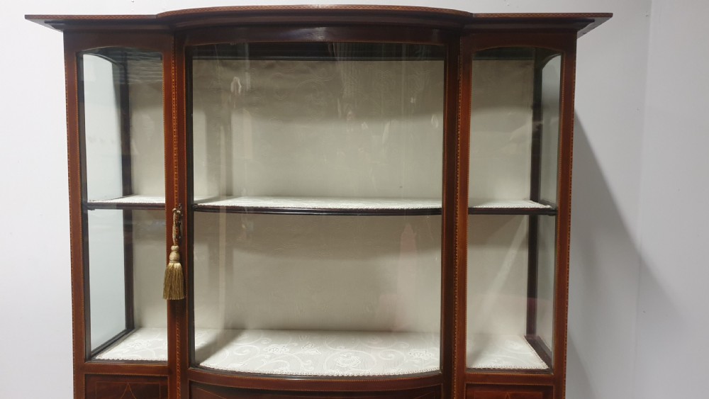 An Edwardian inlaid mahogany display cabinet featuring glazed doors, string marquetry details, and slender tapered legs connected by a lower shelf. View V