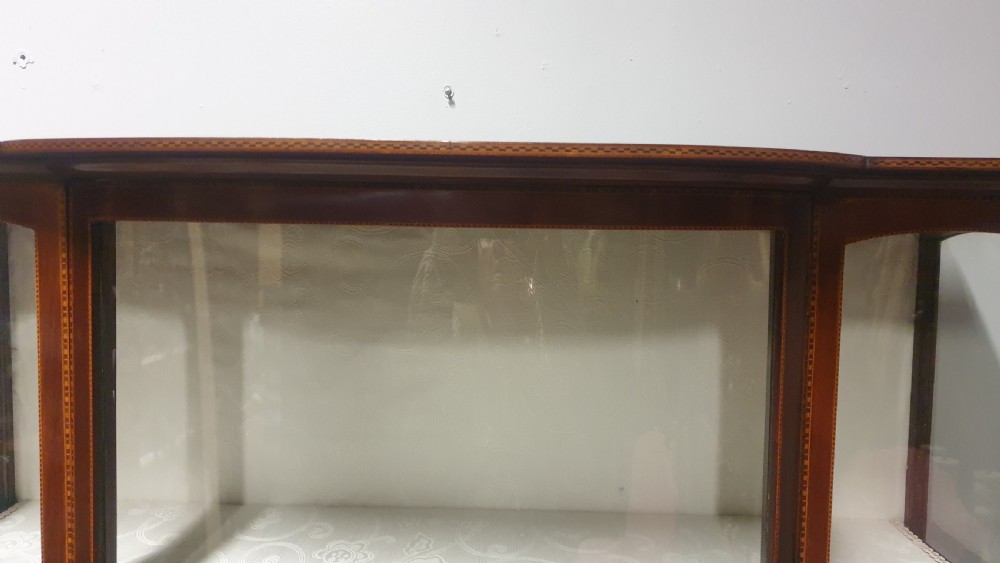 An Edwardian inlaid mahogany display cabinet featuring glazed doors, string marquetry details, and slender tapered legs connected by a lower shelf. View VI