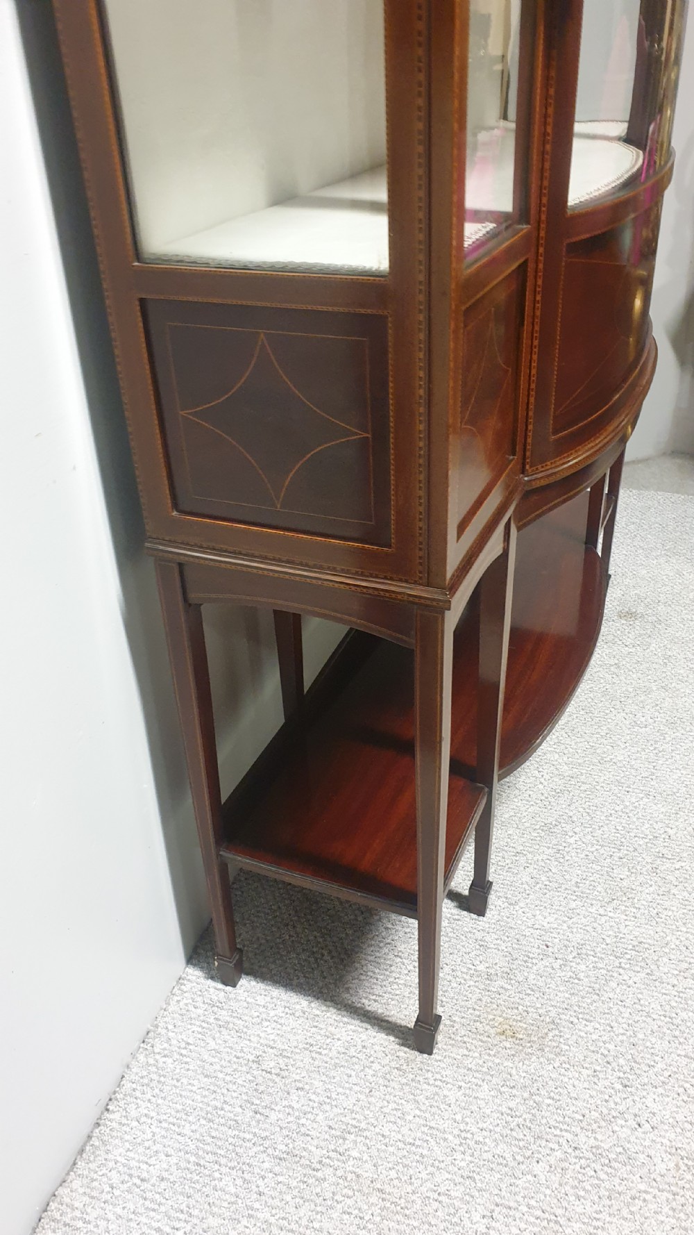 An Edwardian inlaid mahogany display cabinet featuring glazed doors, string marquetry details, and slender tapered legs connected by a lower shelf. View VII