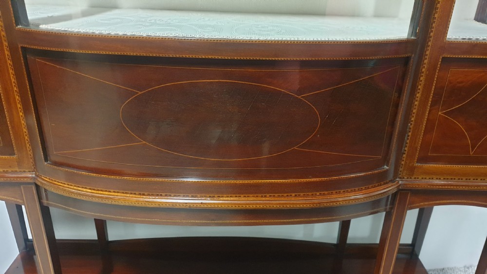 An Edwardian inlaid mahogany display cabinet featuring glazed doors, string marquetry details, and slender tapered legs connected by a lower shelf. View VIII