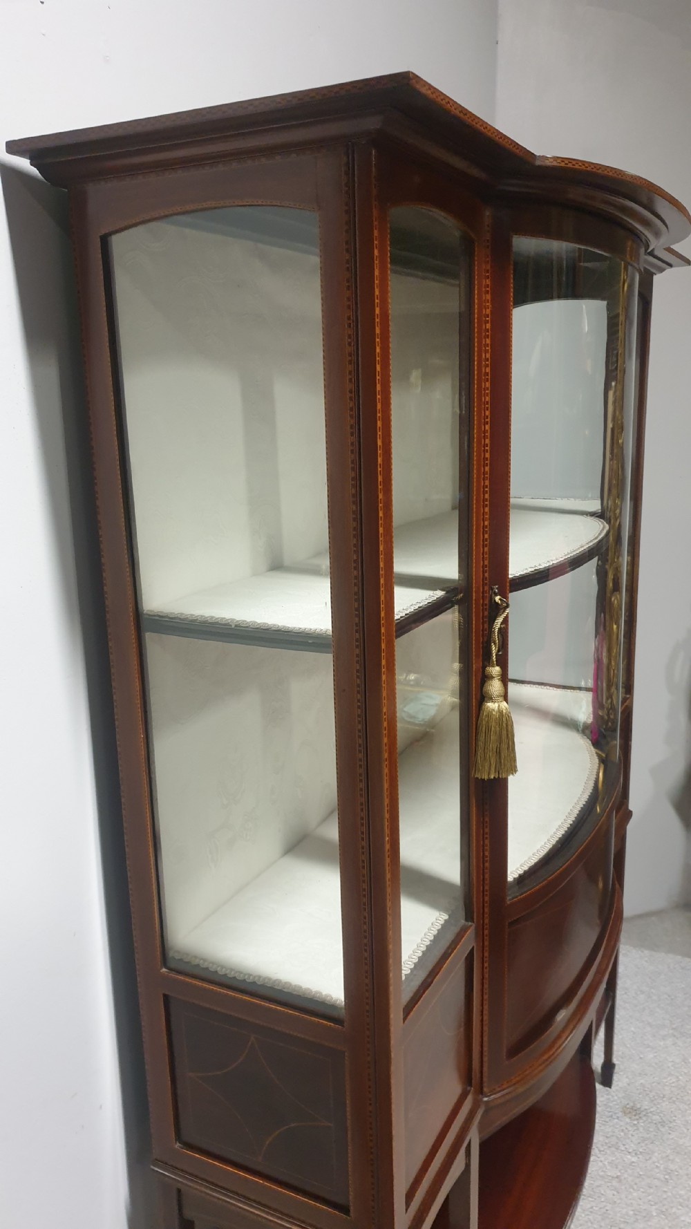 An Edwardian inlaid mahogany display cabinet featuring glazed doors, string marquetry details, and slender tapered legs connected by a lower shelf. View X