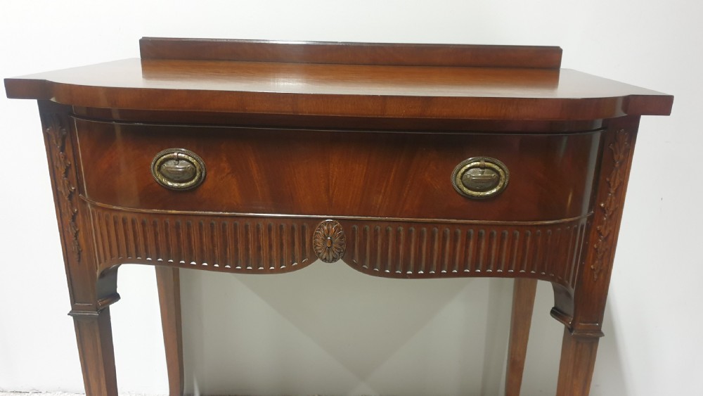 A small mahogany sideboard featuring a single curved drawer, brass ring handles, and fluted tapered legs. View V