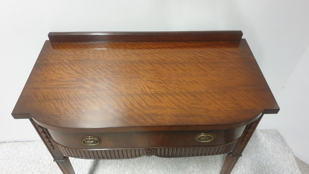 A small mahogany sideboard featuring a single curved drawer, brass ring handles, and fluted tapered legs. View VI