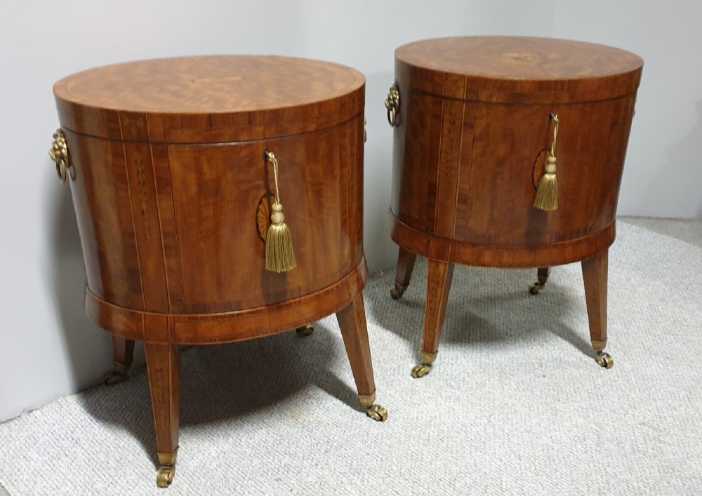 A pair of cylindrical satinwood wine coolers featuring inlaid marquetry oval medallions, lion mask brass side handles, key tassels, tapered legs, and brass castors. View II