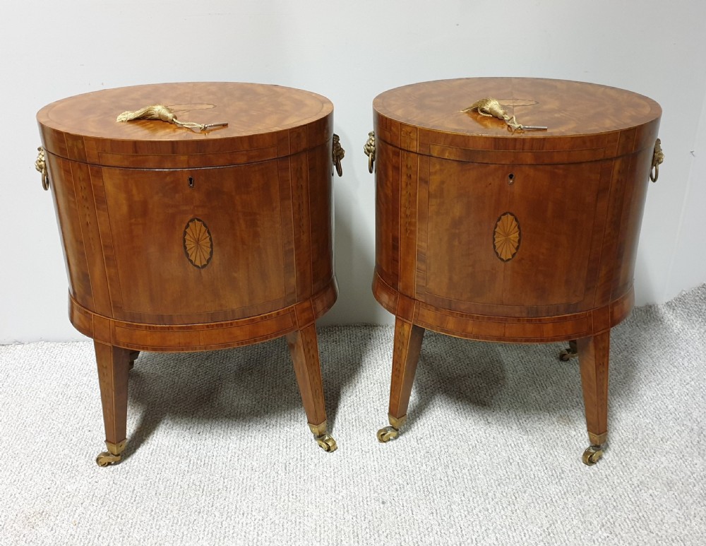 A pair of cylindrical satinwood wine coolers featuring inlaid marquetry oval medallions, lion mask brass side handles, key tassels, tapered legs, and brass castors. View III