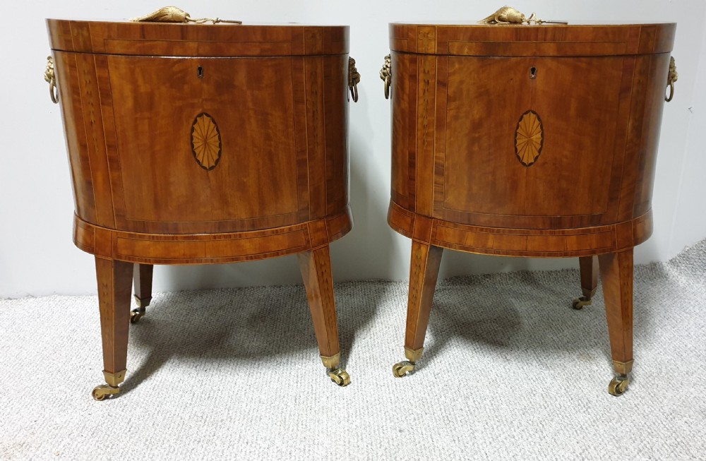 A pair of cylindrical satinwood wine coolers featuring inlaid marquetry oval medallions, lion mask brass side handles, key tassels, tapered legs, and brass castors. View IV