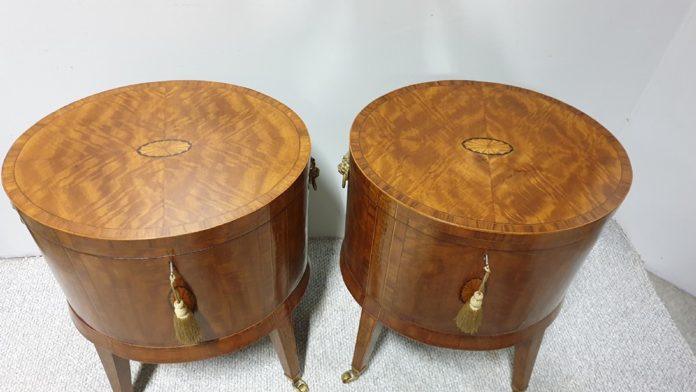A pair of cylindrical satinwood wine coolers featuring inlaid marquetry oval medallions, lion mask brass side handles, key tassels, tapered legs, and brass castors. View V