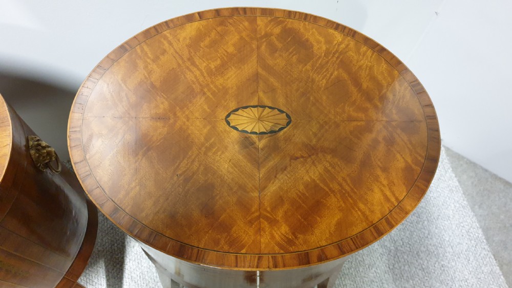 A pair of cylindrical satinwood wine coolers featuring inlaid marquetry oval medallions, lion mask brass side handles, key tassels, tapered legs, and brass castors. View VII