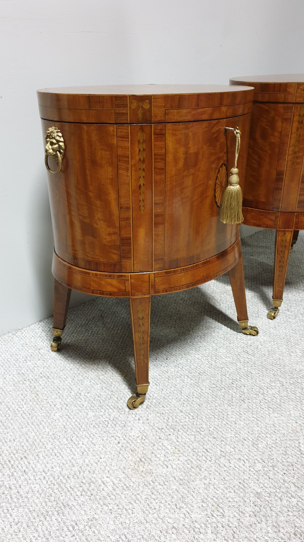 A pair of cylindrical satinwood wine coolers featuring inlaid marquetry oval medallions, lion mask brass side handles, key tassels, tapered legs, and brass castors. View VIII