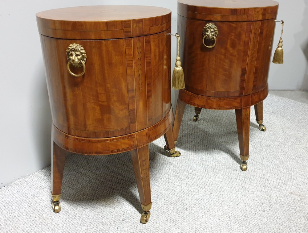 A pair of cylindrical satinwood wine coolers featuring inlaid marquetry oval medallions, lion mask brass side handles, key tassels, tapered legs, and brass castors. View X