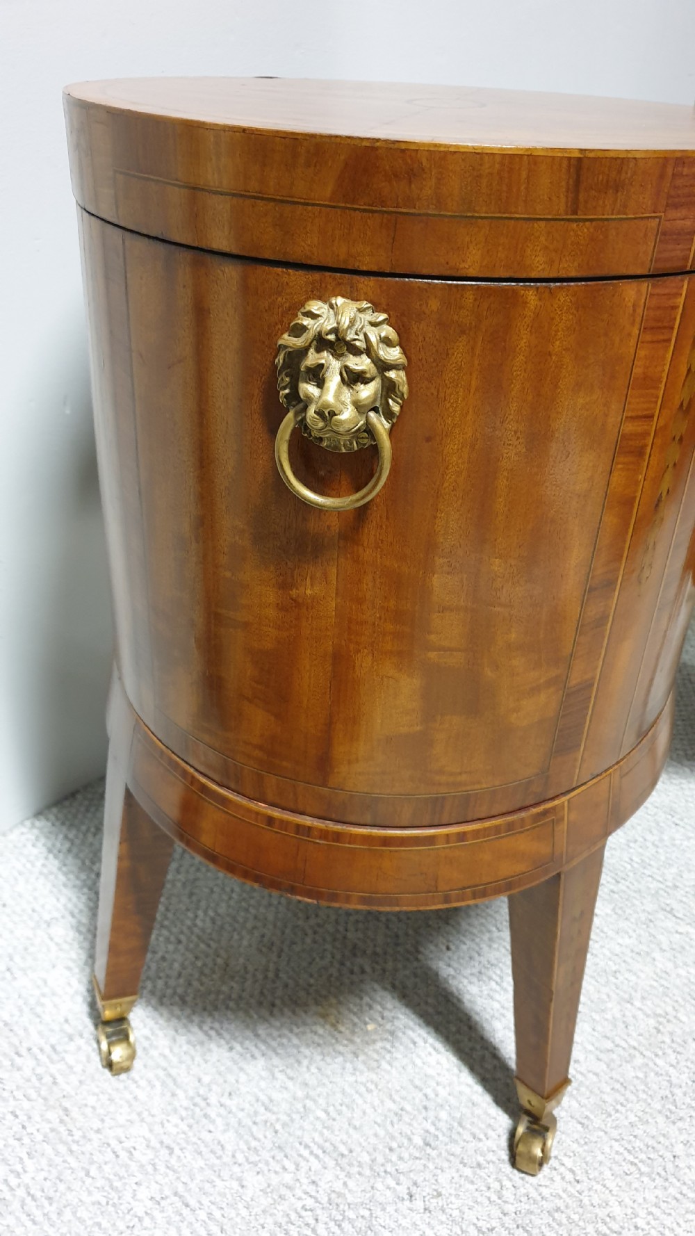 A pair of cylindrical satinwood wine coolers featuring inlaid marquetry oval medallions, lion mask brass side handles, key tassels, tapered legs, and brass castors. View XI