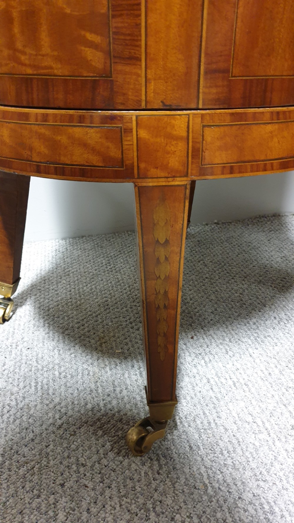 A pair of cylindrical satinwood wine coolers featuring inlaid marquetry oval medallions, lion mask brass side handles, key tassels, tapered legs, and brass castors. View XII