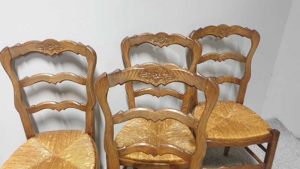A set of four French Provincial oak dining chairs featuring carved floral top rails, wavy ladderbacks, woven rush seats, and cabriole front legs. View II
