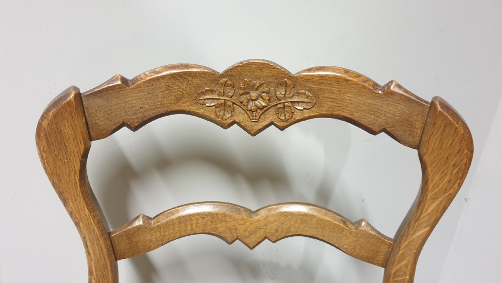 A set of four French Provincial oak dining chairs featuring carved floral top rails, wavy ladderbacks, woven rush seats, and cabriole front legs. View VI