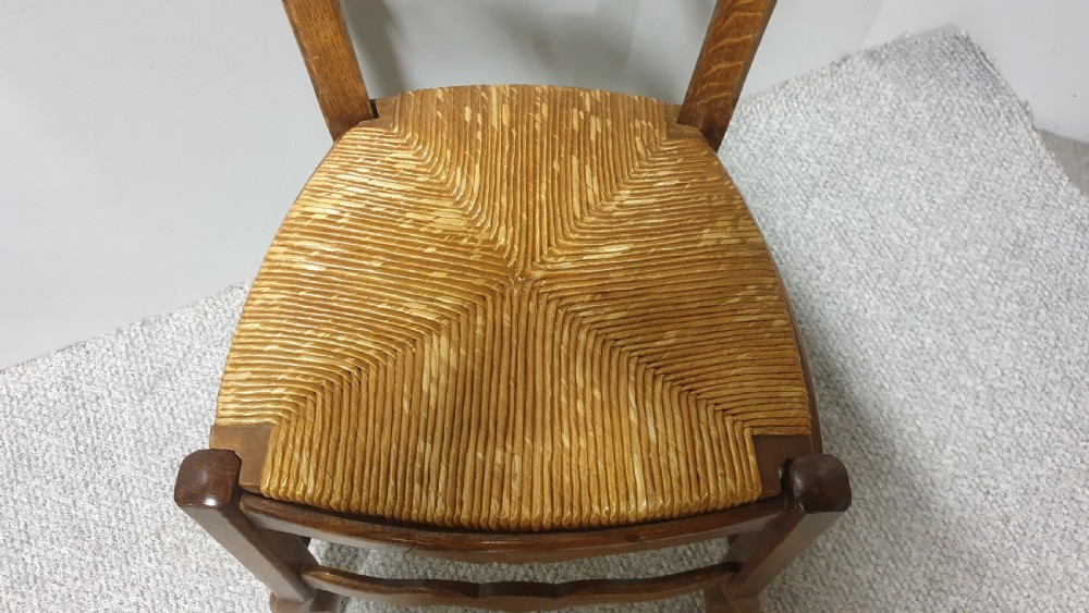 A set of four French Provincial oak dining chairs featuring carved floral top rails, wavy ladderbacks, woven rush seats, and cabriole front legs. View VII