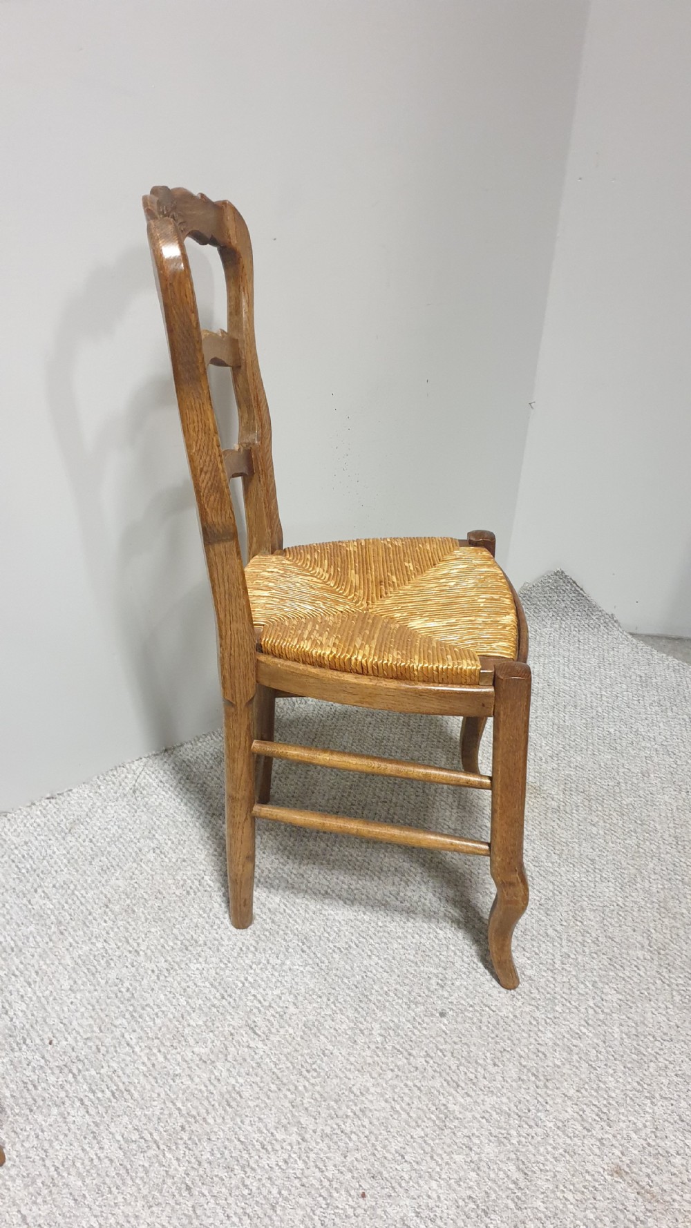 A set of four French Provincial oak dining chairs featuring carved floral top rails, wavy ladderbacks, woven rush seats, and cabriole front legs. View VIII