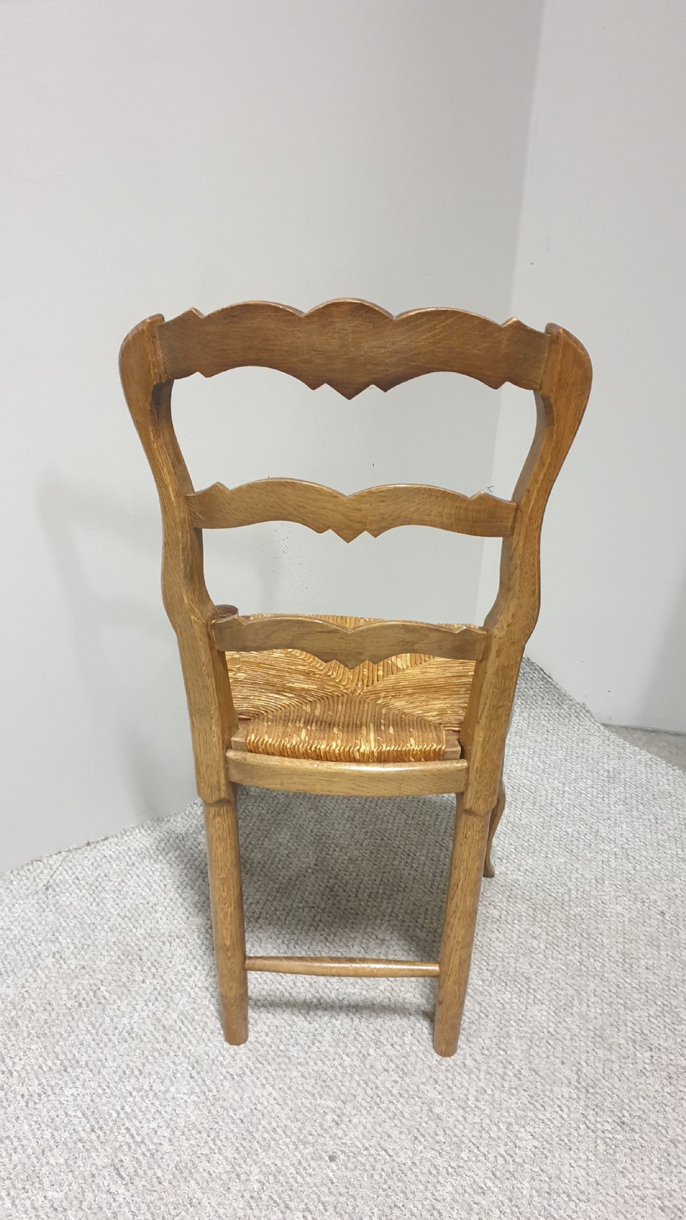 A set of four French Provincial oak dining chairs featuring carved floral top rails, wavy ladderbacks, woven rush seats, and cabriole front legs. View IX