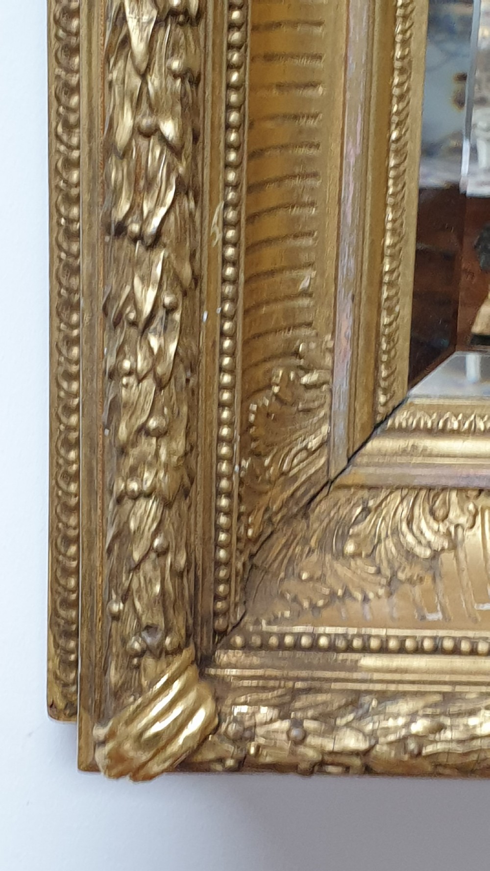 A rectangular antique wall mirror featuring a detailed gold giltwood frame with fluted moulding, leaf trim, and bevelled glass. View V