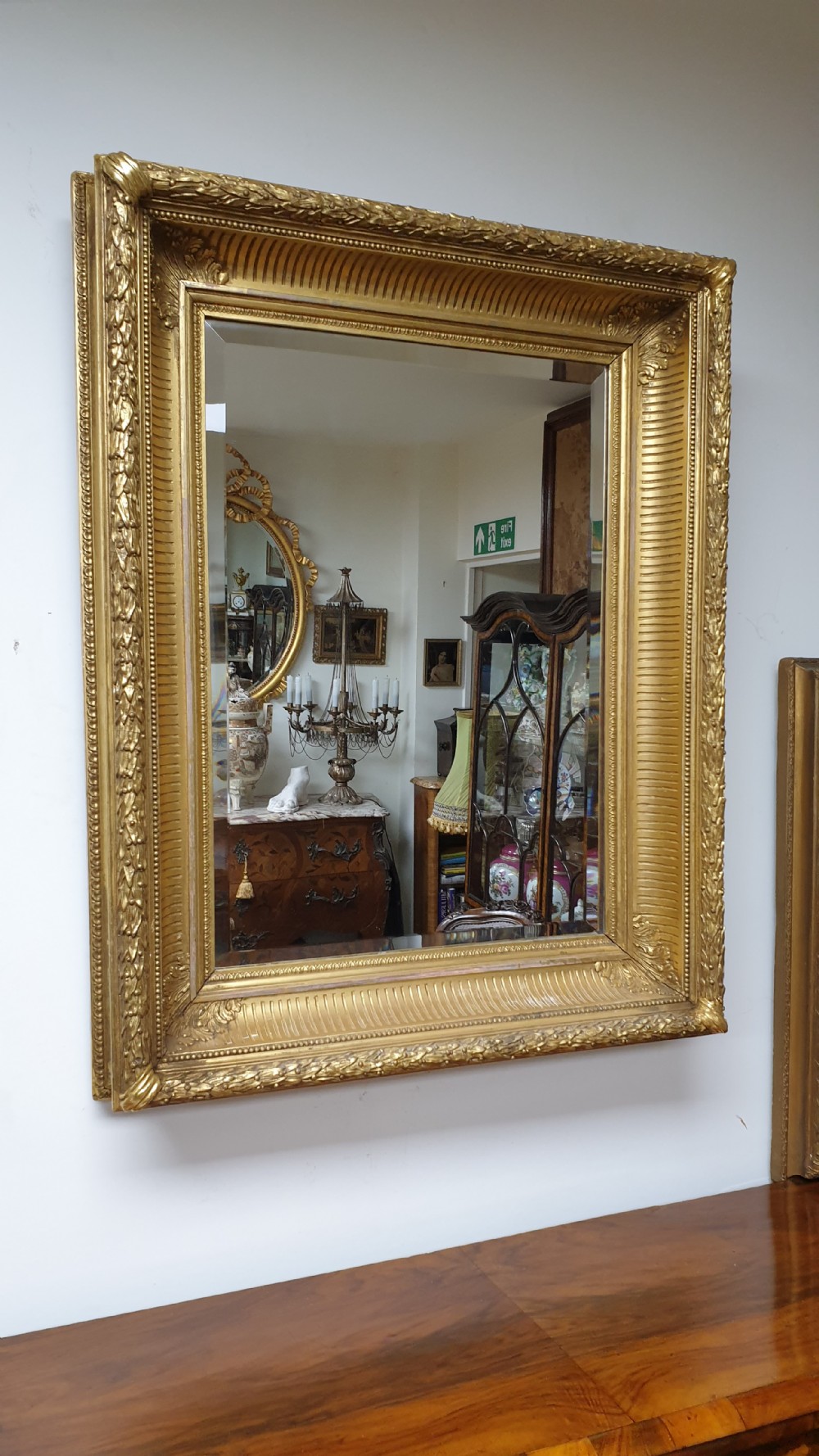 A rectangular antique wall mirror featuring a detailed gold giltwood frame with fluted moulding, leaf trim, and bevelled glass. View X