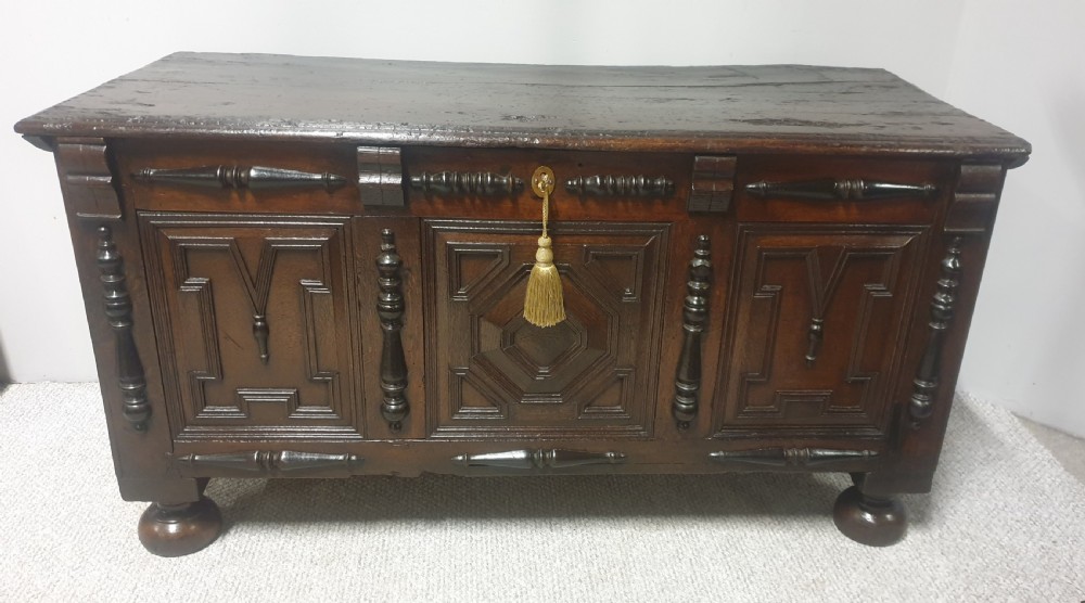 A dark brown carved oak coffer featuring three geometrically moulded front panels, split baluster decoration, and turned bun feet. View II