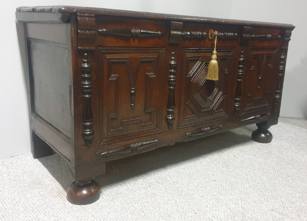 A dark brown carved oak coffer featuring three geometrically moulded front panels, split baluster decoration, and turned bun feet. View III