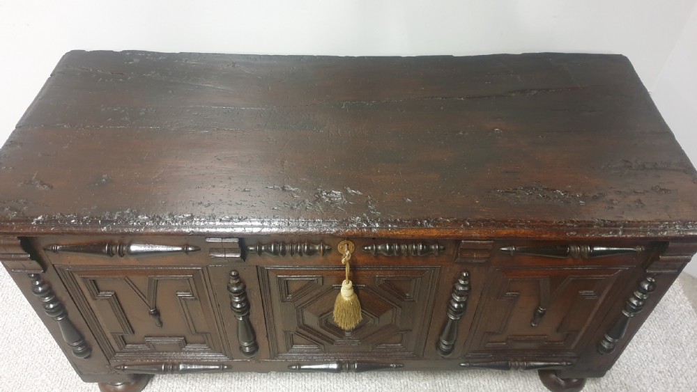 A dark brown carved oak coffer featuring three geometrically moulded front panels, split baluster decoration, and turned bun feet. View IX