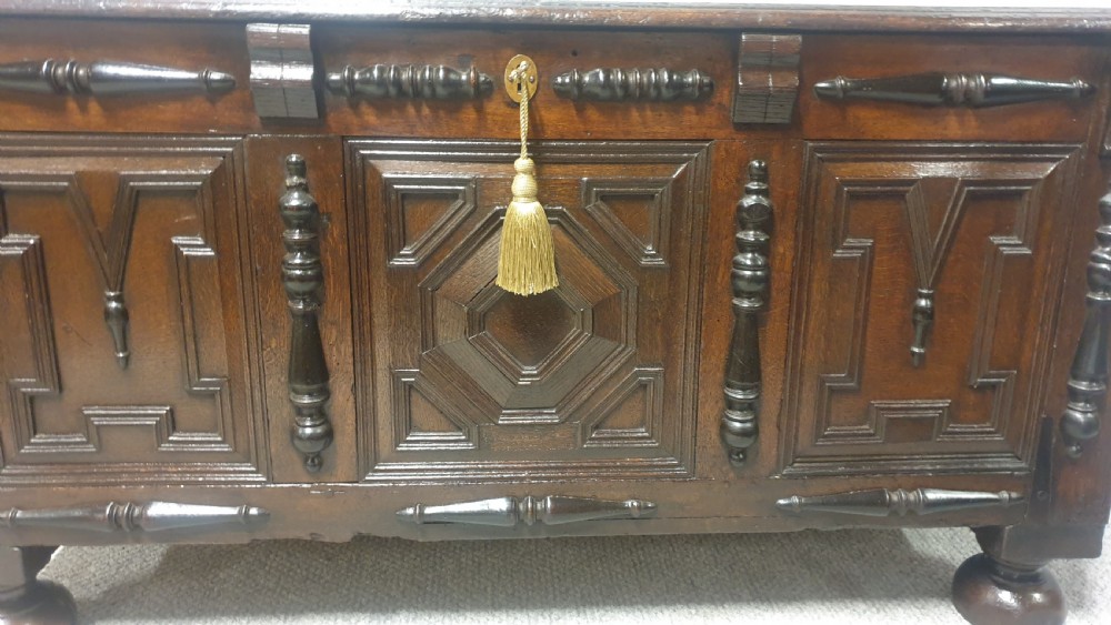A dark brown carved oak coffer featuring three geometrically moulded front panels, split baluster decoration, and turned bun feet. View X