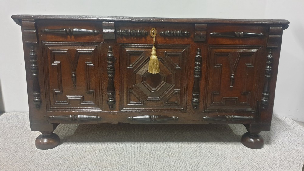 A dark brown carved oak coffer featuring three geometrically moulded front panels, split baluster decoration, and turned bun feet. View XI