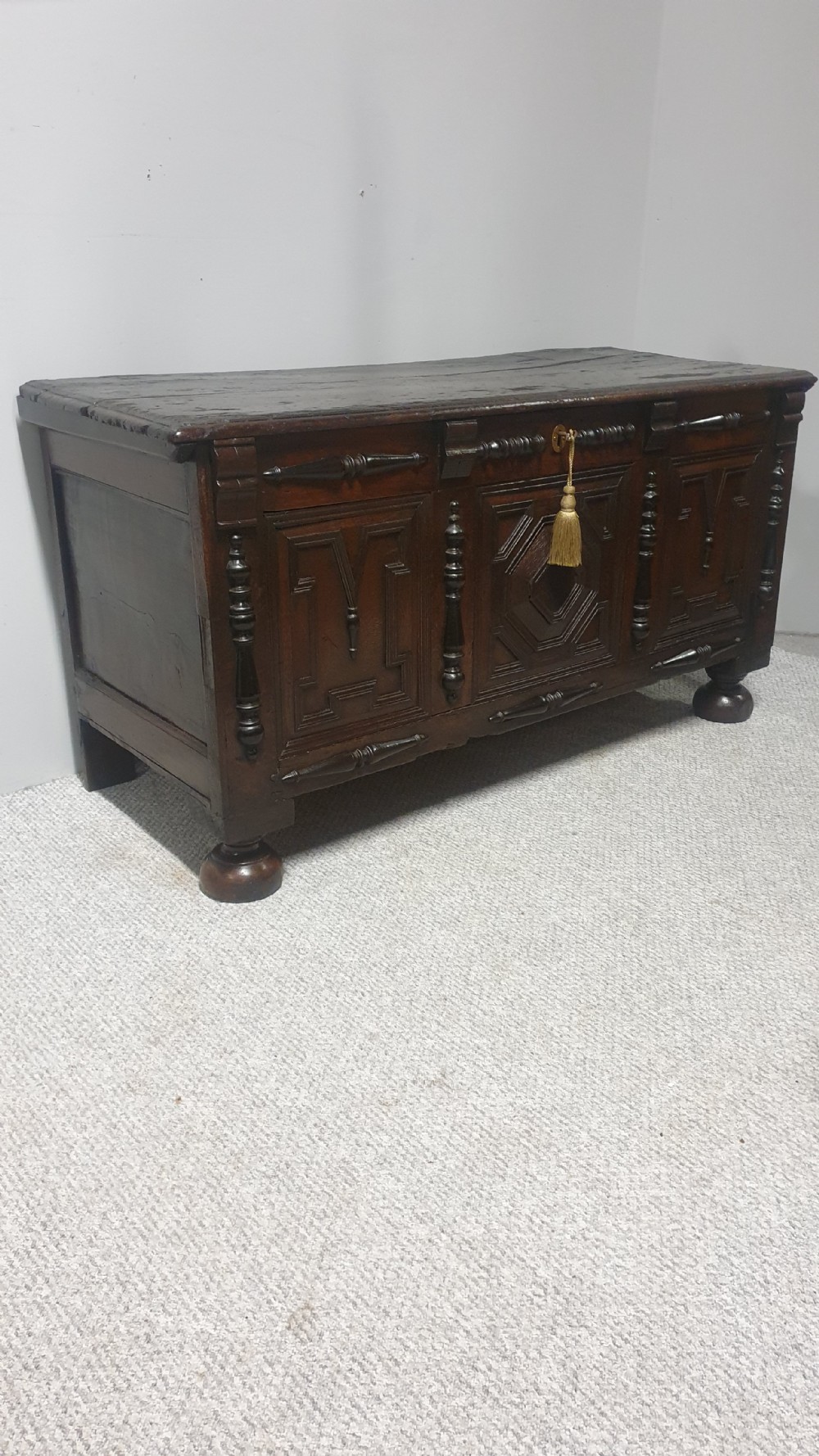 A dark brown carved oak coffer featuring three geometrically moulded front panels, split baluster decoration, and turned bun feet. View XII