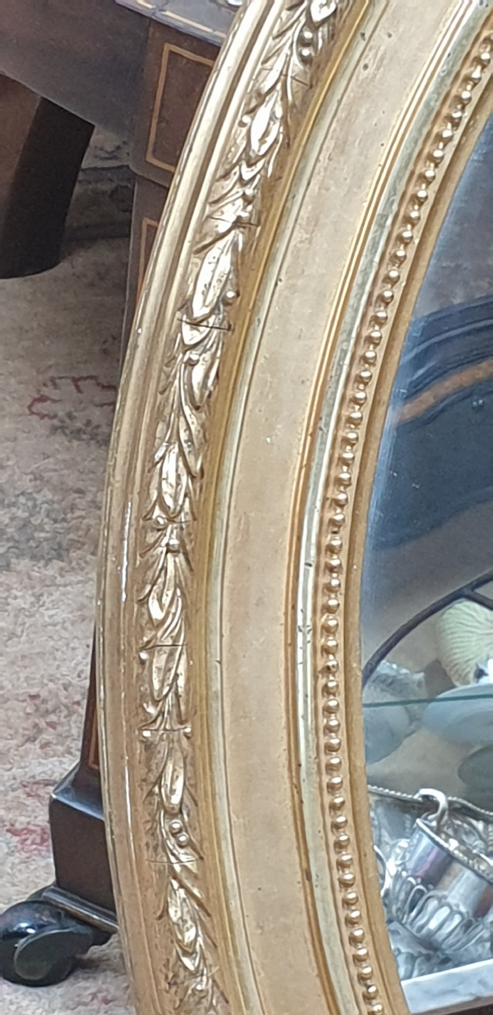 An Edwardian oval wall mirror featuring a gilt frame adorned with carved leaf and bead moulding. View II