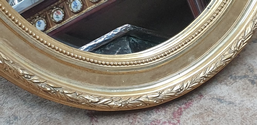 An Edwardian oval wall mirror featuring a gilt frame adorned with carved leaf and bead moulding. View III