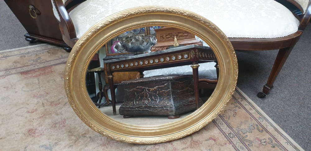 An Edwardian oval wall mirror featuring a gilt frame adorned with carved leaf and bead moulding. View IV