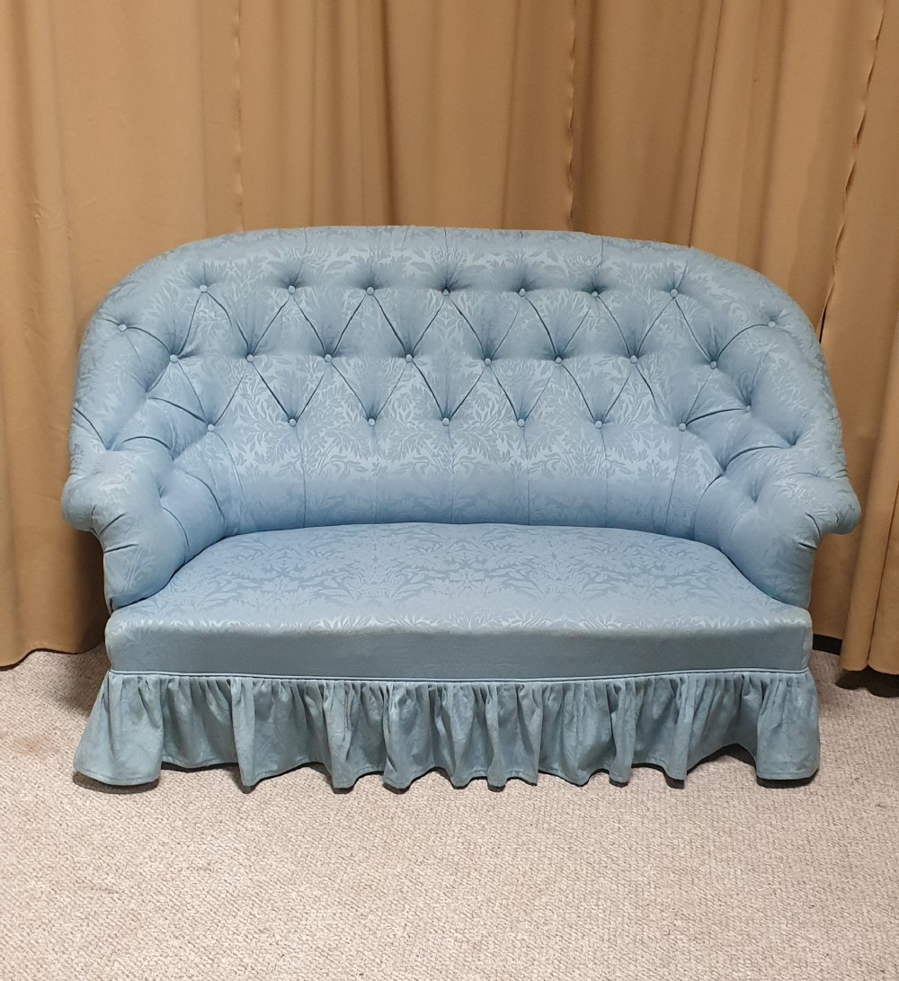 A light blue damask upholstered two-seater settee featuring deep buttoning across the backrest and a pleated base skirt.