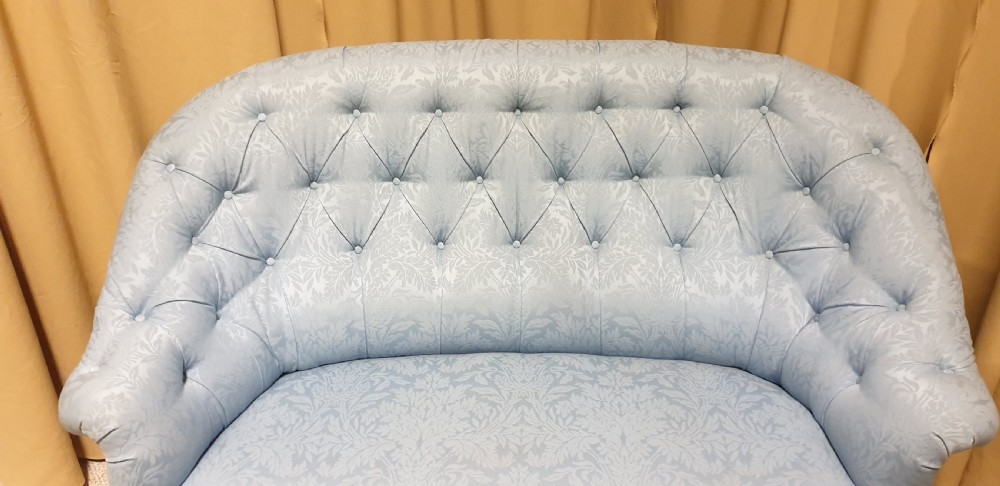 A light blue damask upholstered two-seater settee featuring deep buttoning across the backrest and a pleated base skirt. View III