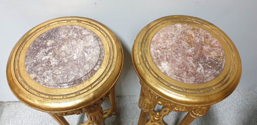 A pair of tall French giltwood torchere stands featuring circular inset marble tops, carved floral aprons, fluted legs, and cross-stretchers with central finials. View II