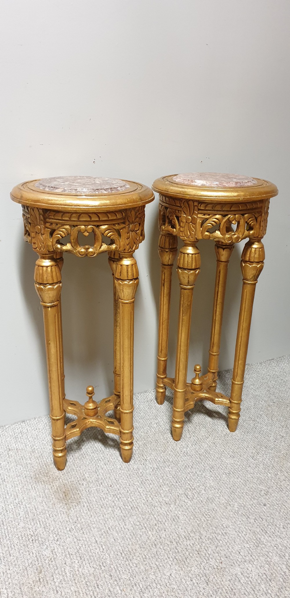 A pair of tall French giltwood torchere stands featuring circular inset marble tops, carved floral aprons, fluted legs, and cross-stretchers with central finials. View VI