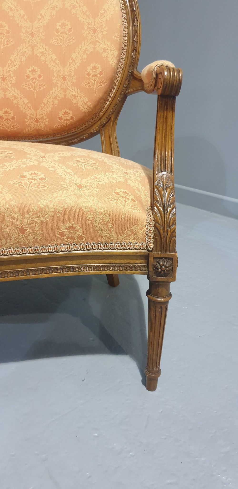 A Louis XVI style French walnut two-seat sofa featuring an oval upholstered backrest, carved timber frame, and turned fluted legs. View V