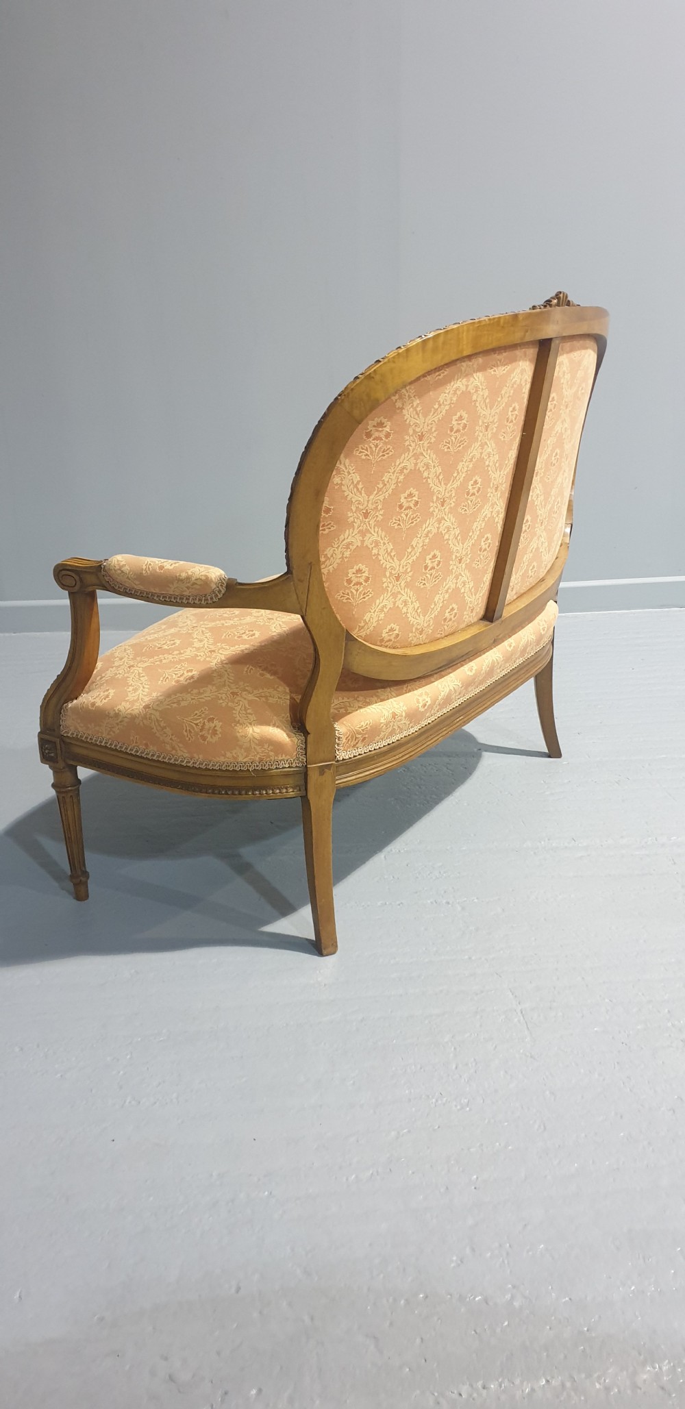 A Louis XVI style French walnut two-seat sofa featuring an oval upholstered backrest, carved timber frame, and turned fluted legs. View IX