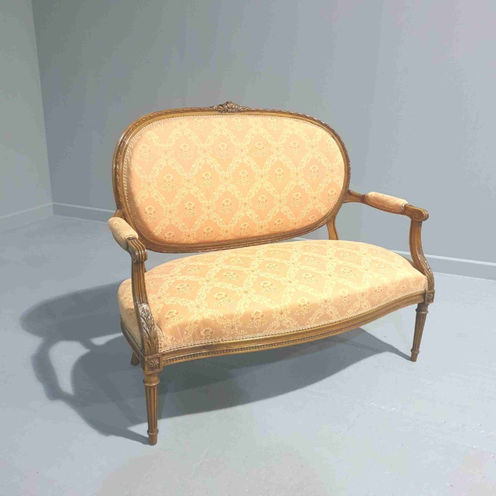 A Louis XVI style French walnut two-seat sofa featuring an oval upholstered backrest, carved timber frame, and turned fluted legs.