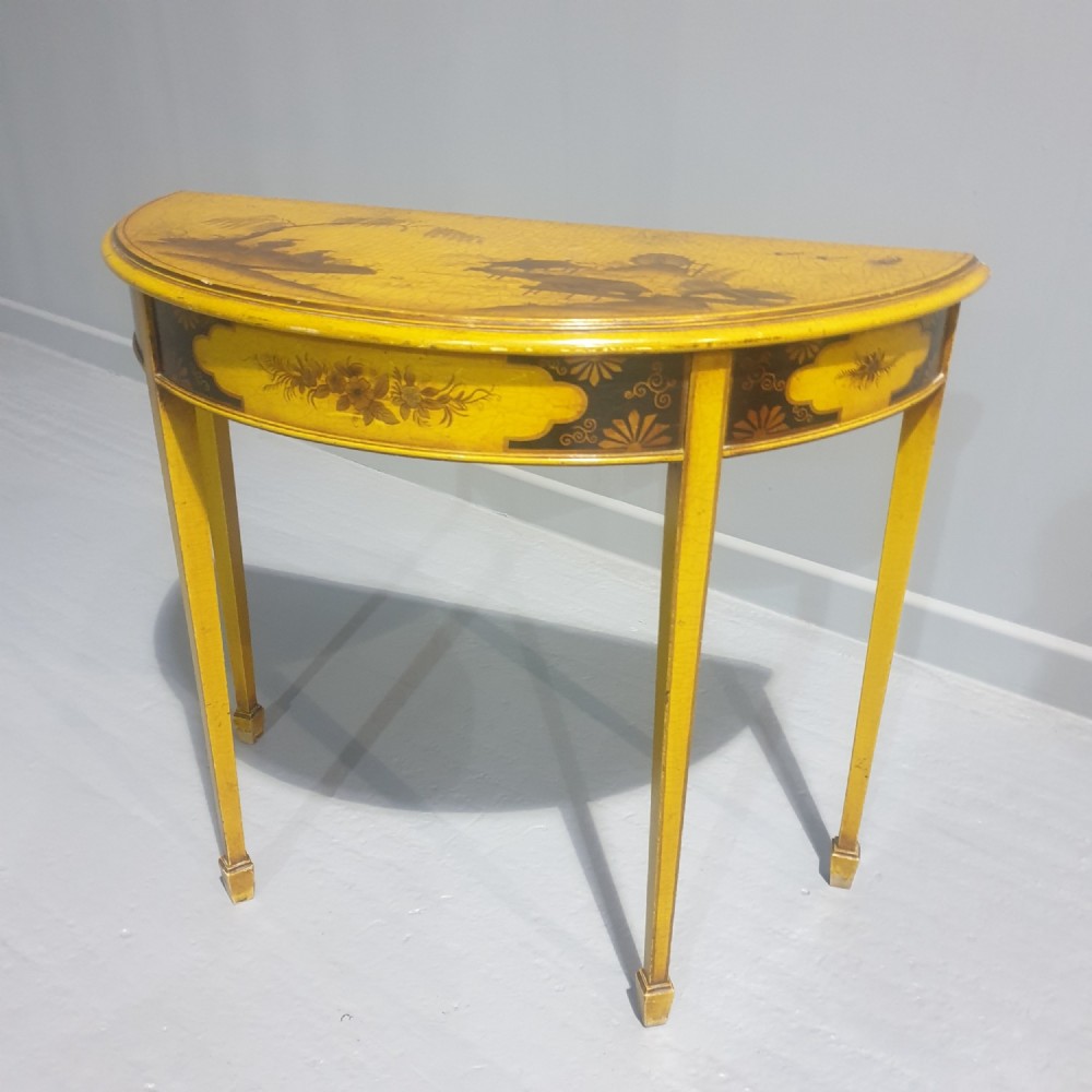 A semicircular yellow lacquered demilune console table featuring hand-painted Chinoiserie landscape detail and slender tapered legs.