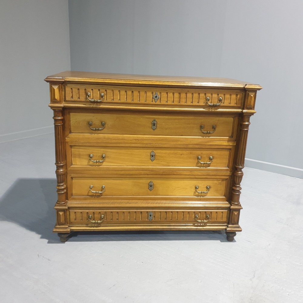 A French walnut chest of drawers featuring five drawers with brass handles, fluted carved top and bottom panels, and turned side columns.