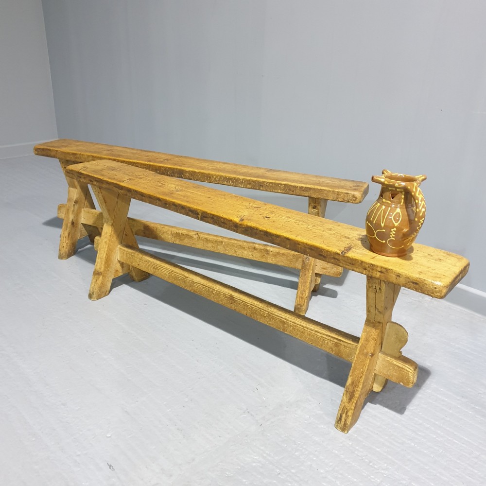 A pair of long rustic pine trestle benches featuring A-frame legs and exposed wooden stretchers.