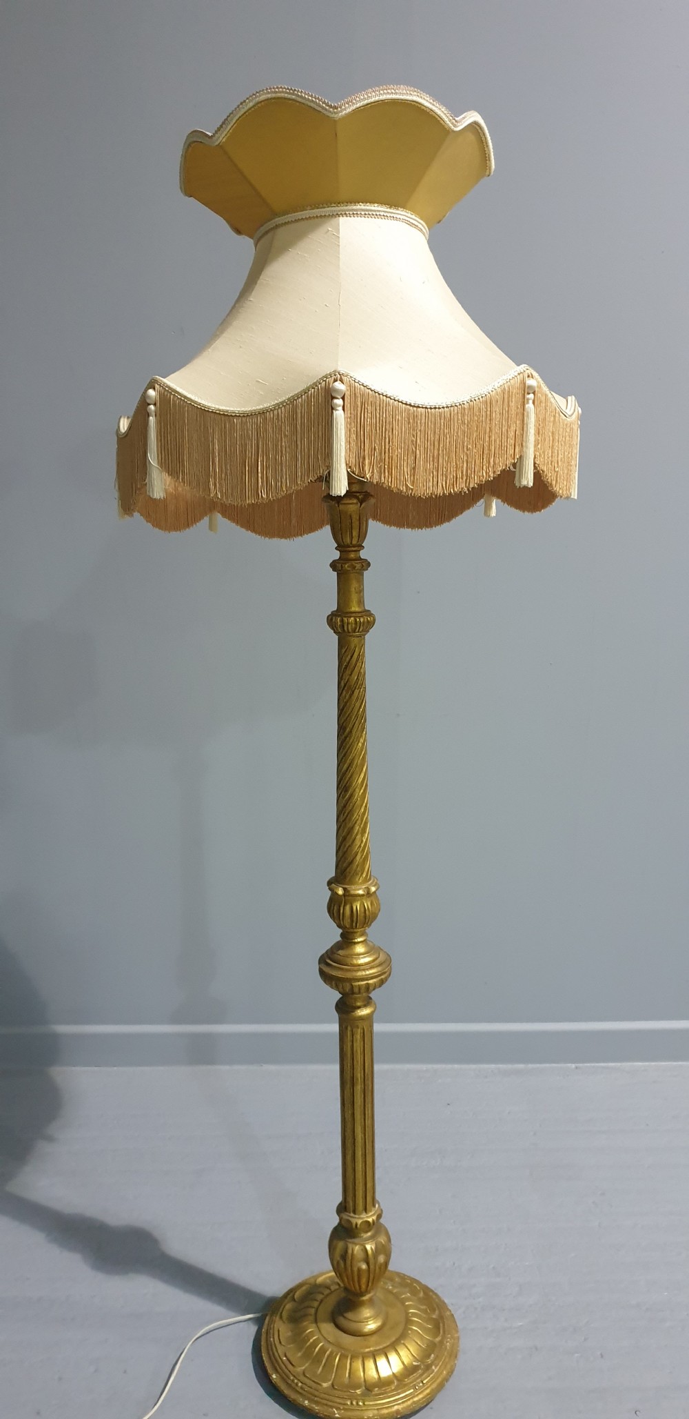 A tall gilded standard lamp featuring a carved fluted column and a cream fabric lampshade trimmed with fringe and tassels. View II
