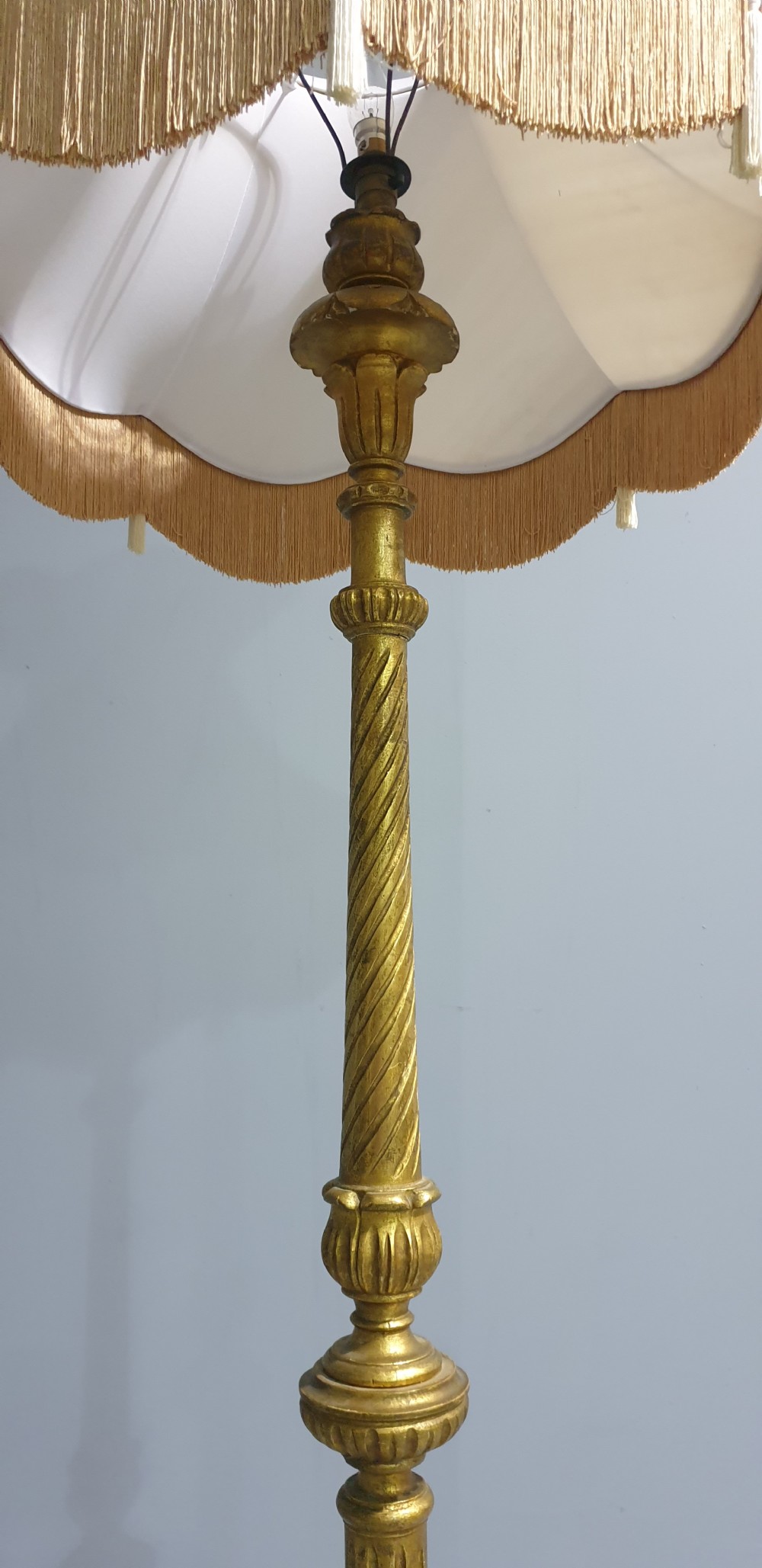 A tall gilded standard lamp featuring a carved fluted column and a cream fabric lampshade trimmed with fringe and tassels. View IV