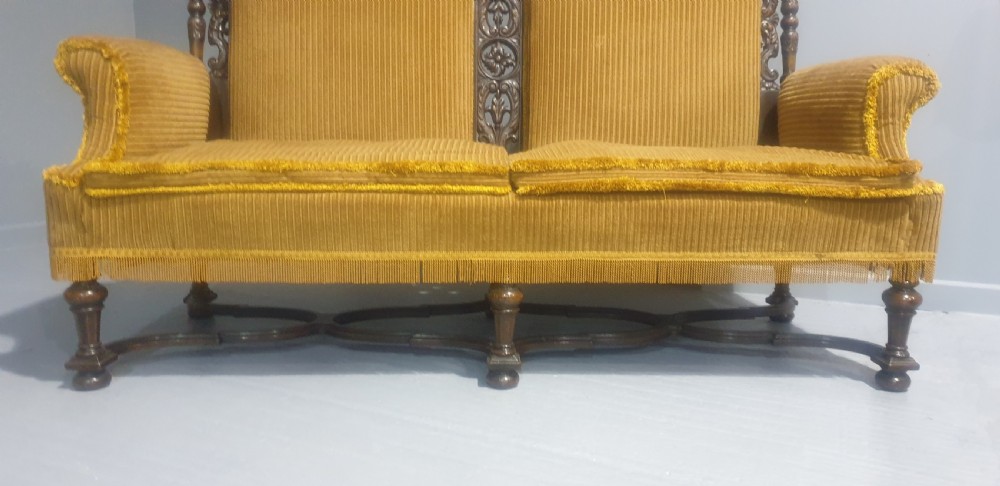 An antique double-backed sofa crafted from dark carved walnut wood with mustard yellow striped upholstery and fringe trim. View III