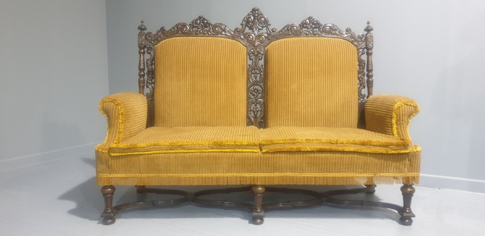 An antique double-backed sofa crafted from dark carved walnut wood with mustard yellow striped upholstery and fringe trim. View V