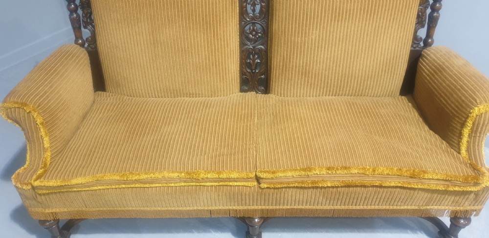 An antique double-backed sofa crafted from dark carved walnut wood with mustard yellow striped upholstery and fringe trim. View VI
