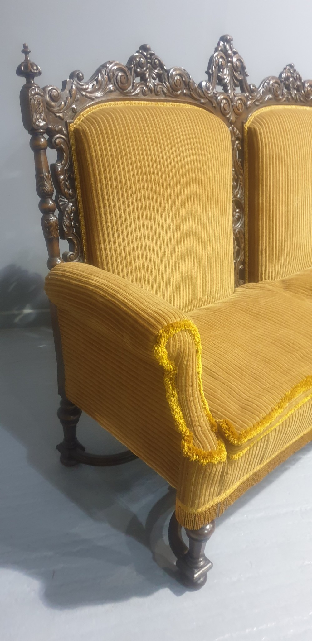 An antique double-backed sofa crafted from dark carved walnut wood with mustard yellow striped upholstery and fringe trim. View VII