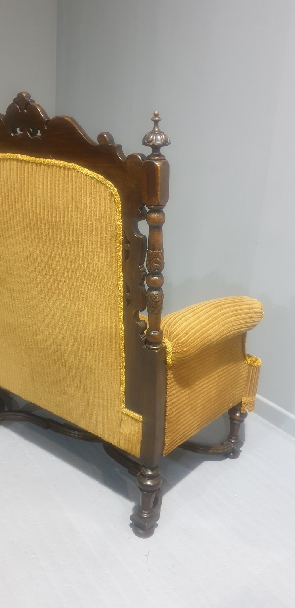 An antique double-backed sofa crafted from dark carved walnut wood with mustard yellow striped upholstery and fringe trim. View IX