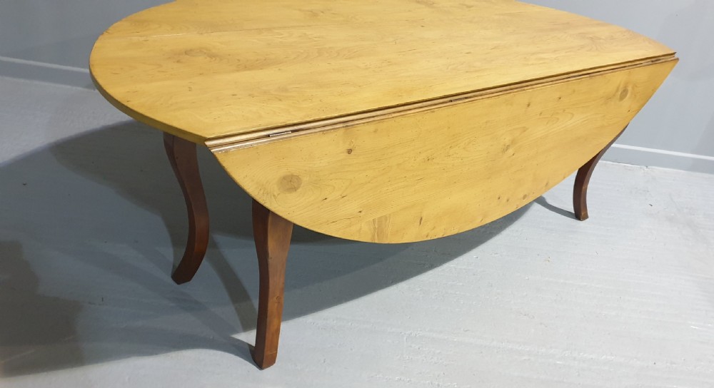 A large French farmhouse dining table featuring a light pine oval top supported by dark fruitwood cabriole legs. View V